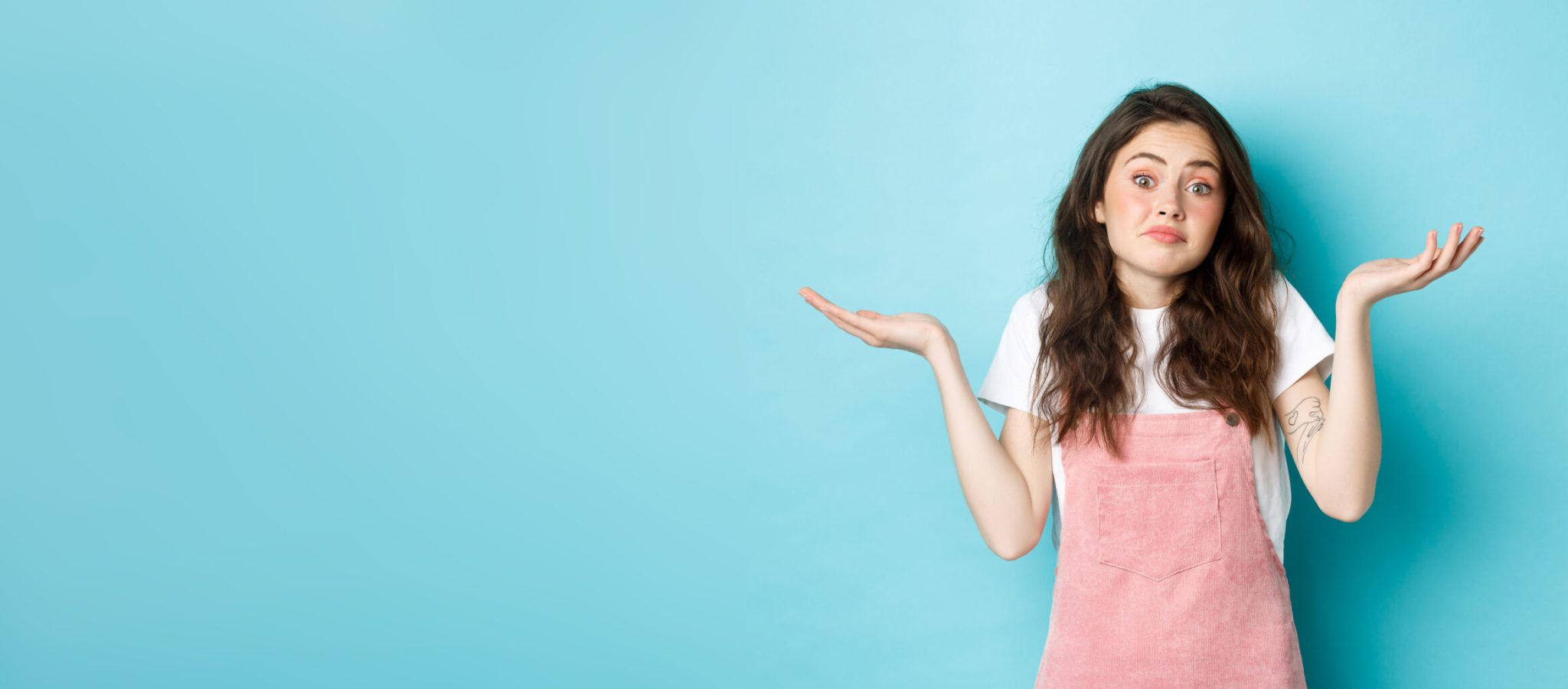 Portrait of confused cute brunette girl shrugging shoulders, know nothing, cant tell, standing indecisive against blue background.